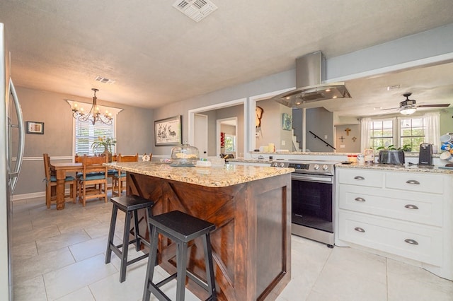 kitchen featuring island exhaust hood, decorative light fixtures, white cabinets, ceiling fan with notable chandelier, and appliances with stainless steel finishes