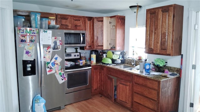 kitchen featuring light wood finished floors, stone countertops, appliances with stainless steel finishes, pendant lighting, and a sink