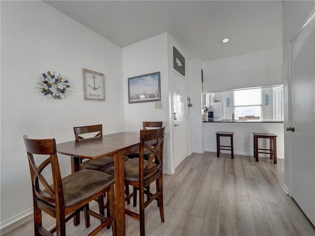 dining area with a textured ceiling and light hardwood / wood-style flooring