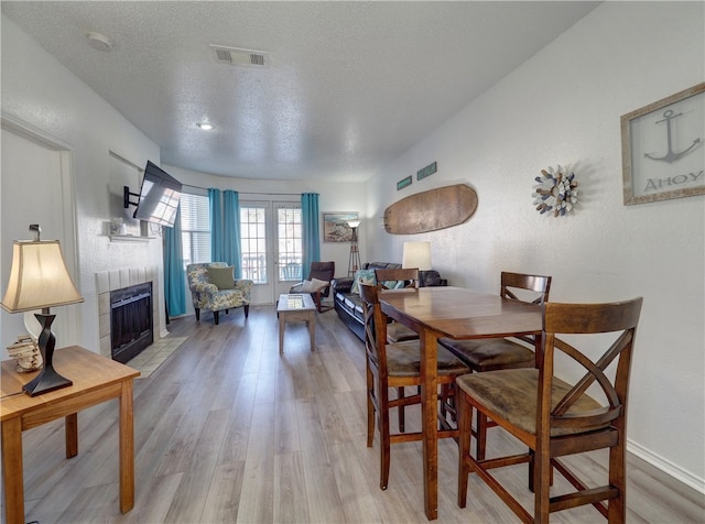 dining space with french doors, wood-type flooring, a textured ceiling, and a tiled fireplace