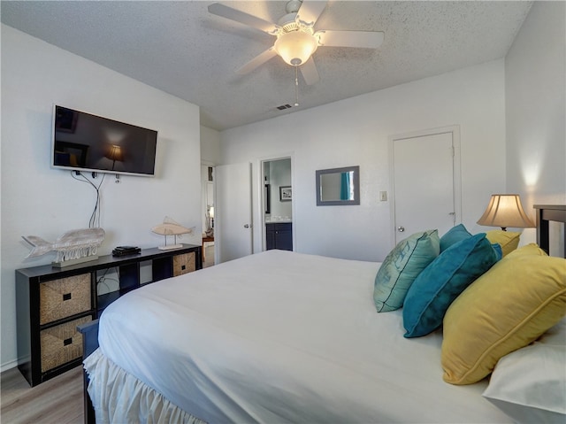 bedroom with ensuite bath, a textured ceiling, ceiling fan, and light hardwood / wood-style flooring