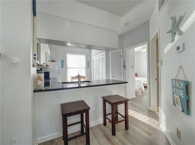 kitchen with white cabinetry, a kitchen bar, sink, light hardwood / wood-style floors, and kitchen peninsula