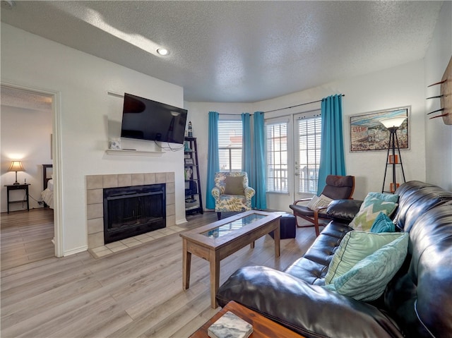 living room with a tiled fireplace, a textured ceiling, and wood-type flooring