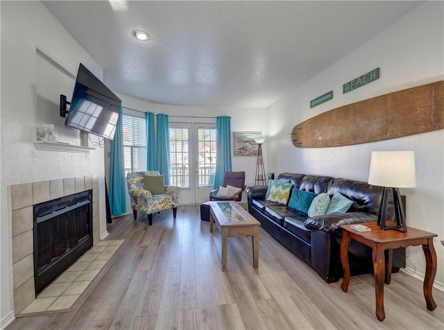 living room featuring a tiled fireplace, a textured ceiling, and light hardwood / wood-style floors