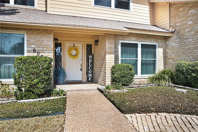 entrance to property with a shingled roof and brick siding