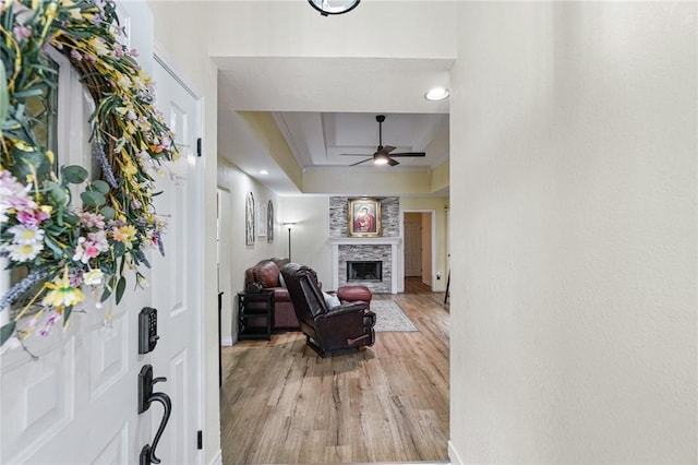 entrance foyer with crown molding, a large fireplace, a tray ceiling, light wood-style flooring, and a ceiling fan