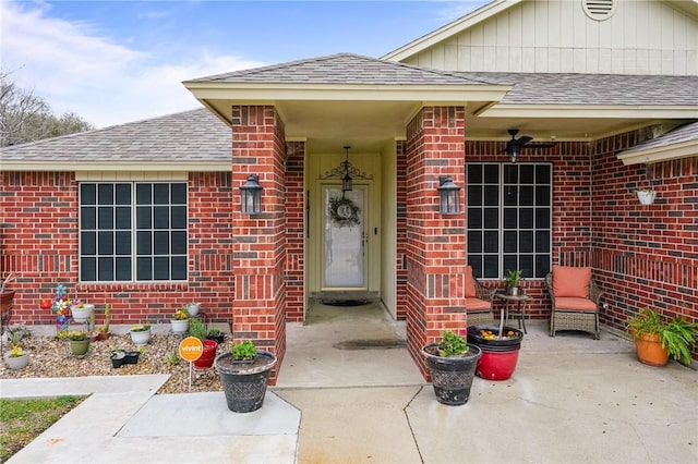 view of exterior entry with brick siding and a shingled roof