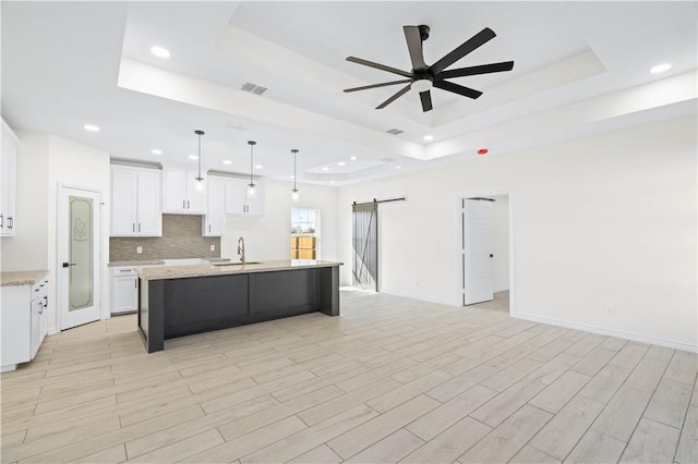 kitchen featuring a barn door, a kitchen island with sink, visible vents, open floor plan, and a raised ceiling