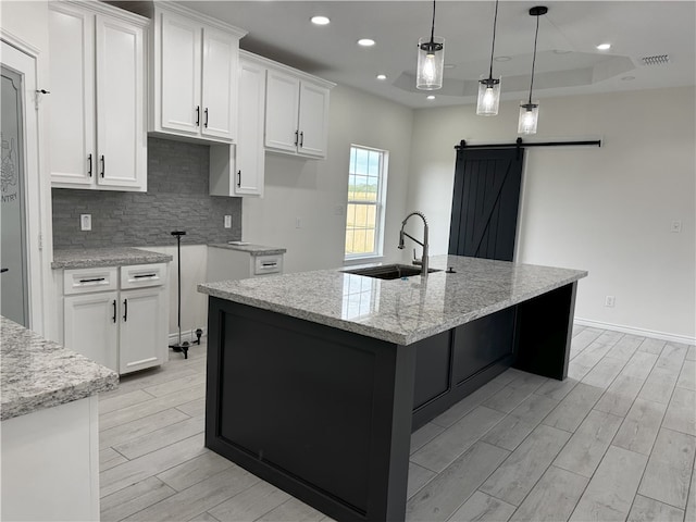 kitchen with decorative light fixtures, a barn door, white cabinetry, and an island with sink