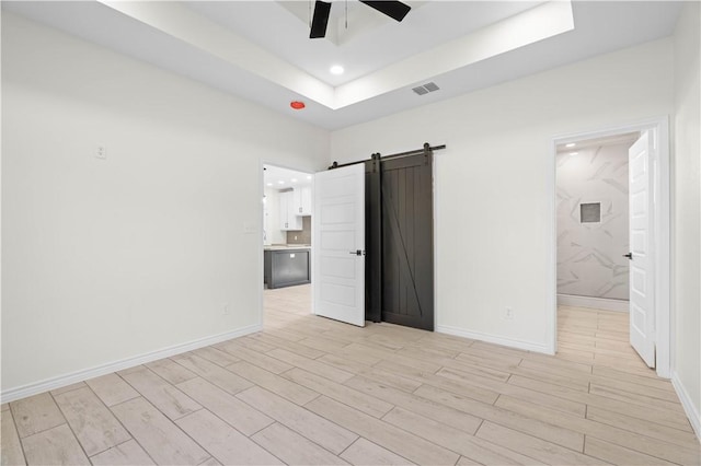 unfurnished room featuring a barn door, visible vents, baseboards, light wood-type flooring, and a tray ceiling