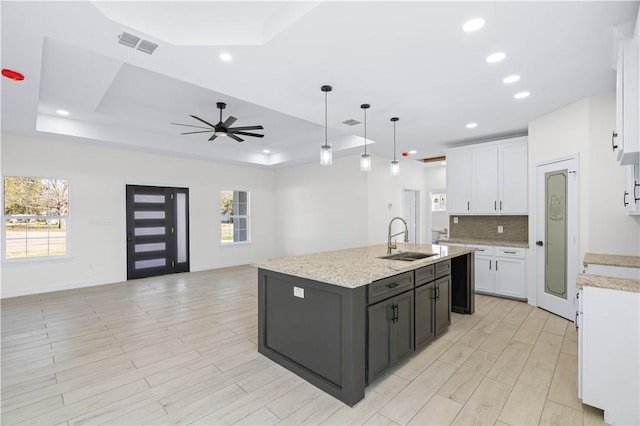 kitchen featuring a sink, visible vents, white cabinetry, a tray ceiling, and an island with sink