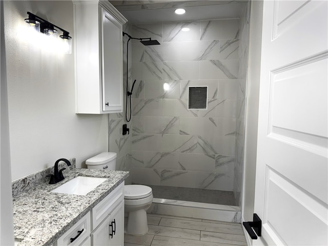 bathroom featuring a tile shower, vanity, and toilet