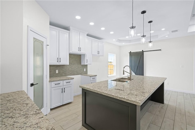 kitchen featuring a barn door, a sink, wood finish floors, white cabinetry, and backsplash