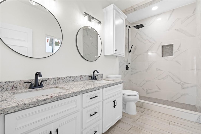 full bath with double vanity, tiled shower, a sink, and toilet