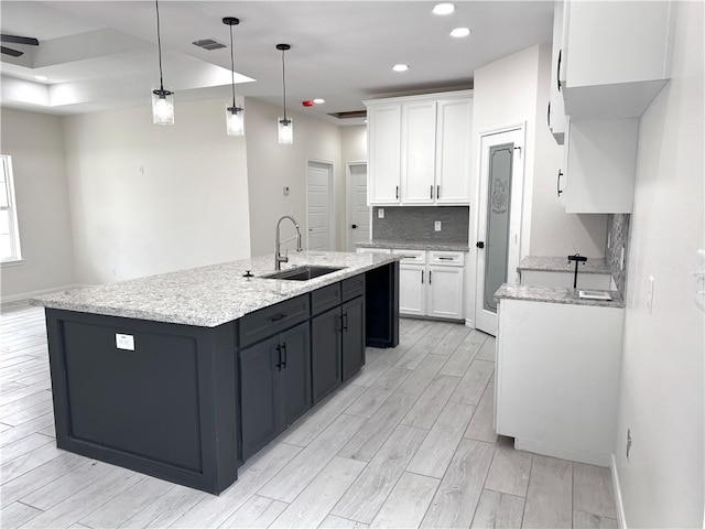 kitchen featuring white cabinets, pendant lighting, sink, and an island with sink