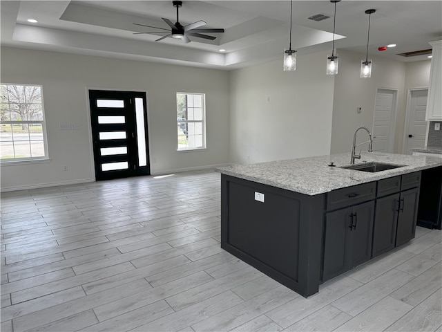 kitchen with light stone counters, a tray ceiling, ceiling fan, sink, and hanging light fixtures