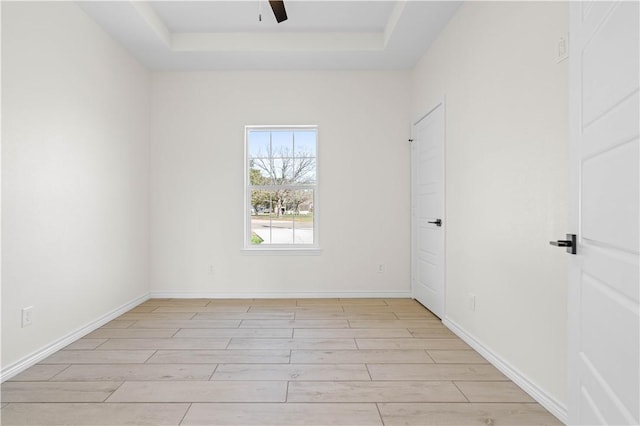 unfurnished room with ceiling fan, a raised ceiling, light wood-style flooring, and baseboards