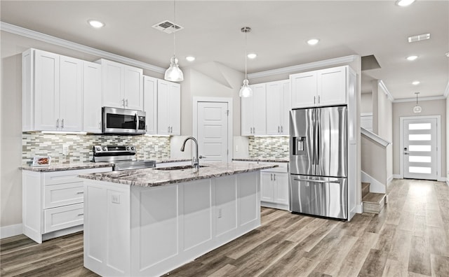 kitchen featuring appliances with stainless steel finishes, an island with sink, sink, white cabinets, and light stone counters