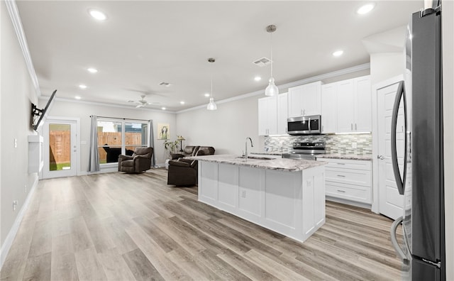 kitchen featuring pendant lighting, white cabinets, stainless steel appliances, light stone countertops, and a center island with sink