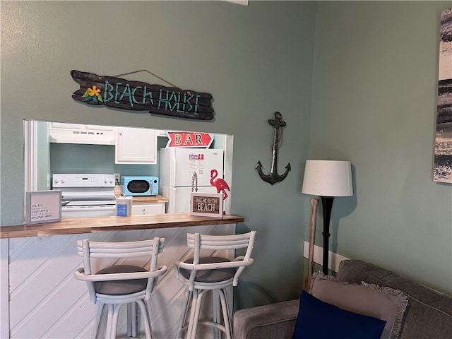 interior space featuring wooden counters, exhaust hood, white appliances, and a breakfast bar