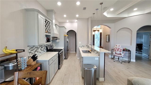 kitchen featuring hanging light fixtures, sink, backsplash, light wood-type flooring, and appliances with stainless steel finishes