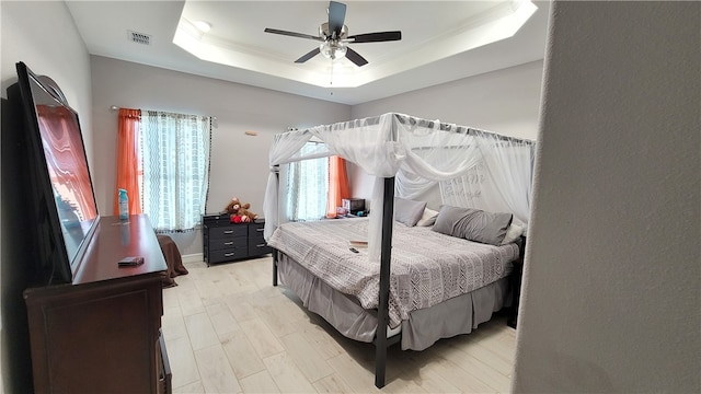 bedroom featuring ceiling fan, multiple windows, and a raised ceiling