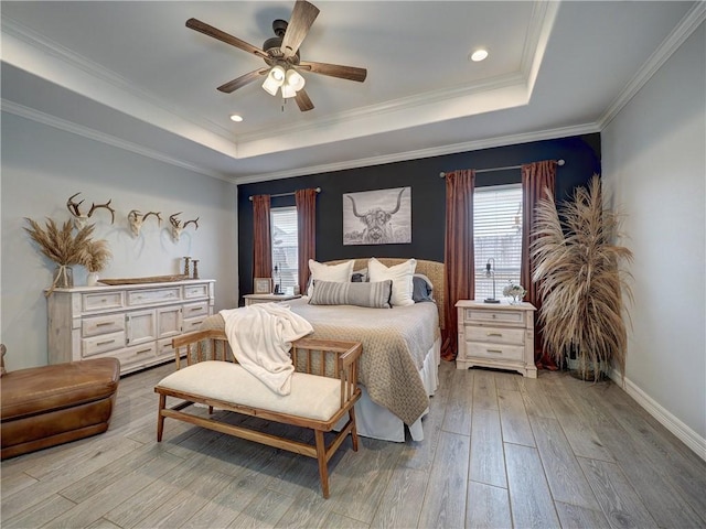 bedroom featuring light wood-style flooring, multiple windows, a tray ceiling, and ornamental molding