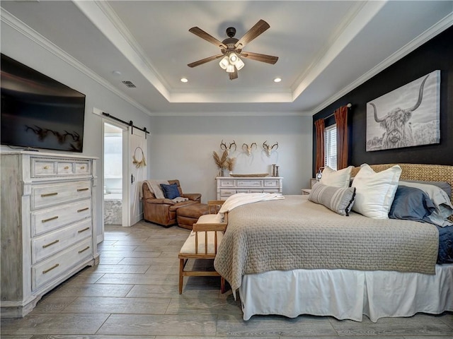 bedroom featuring a tray ceiling, visible vents, a barn door, ornamental molding, and light wood-type flooring