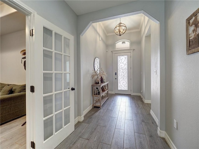 entrance foyer featuring arched walkways, wood finished floors, baseboards, ornamental molding, and an inviting chandelier