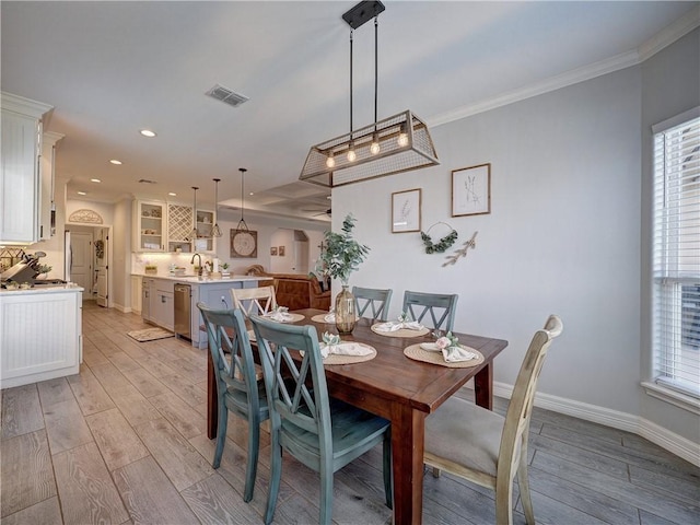 dining space with light wood-type flooring, baseboards, visible vents, and crown molding