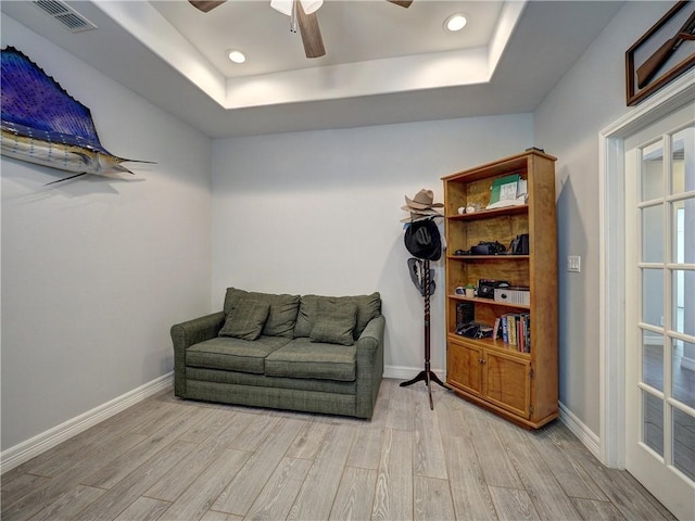 sitting room with light wood-style floors, a tray ceiling, visible vents, and baseboards