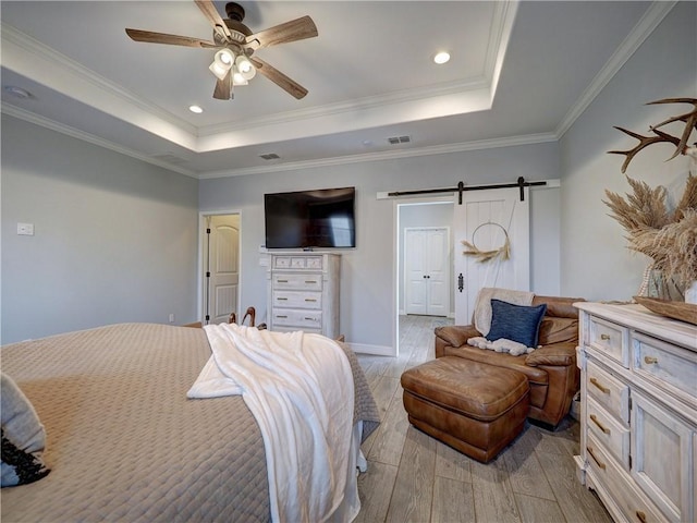 bedroom featuring a tray ceiling, visible vents, a barn door, light wood-style floors, and ornamental molding