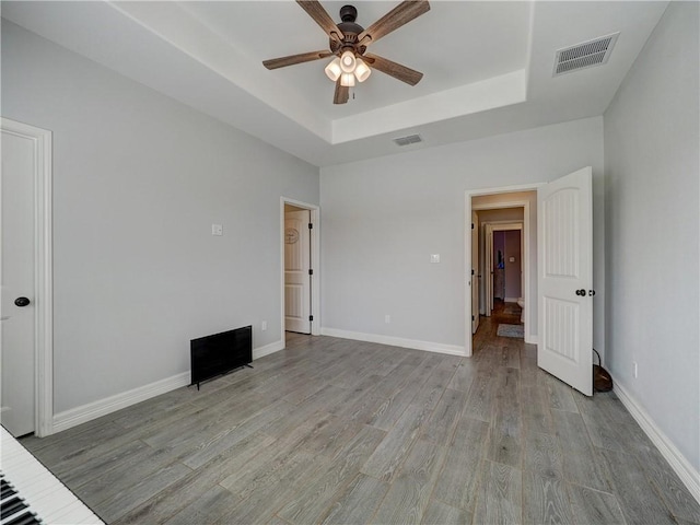 unfurnished bedroom with a tray ceiling, baseboards, visible vents, and light wood finished floors