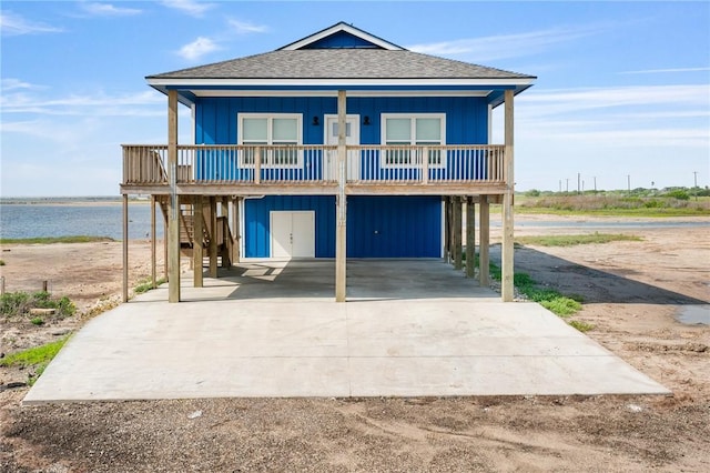 coastal home featuring a water view, roof with shingles, concrete driveway, and a carport