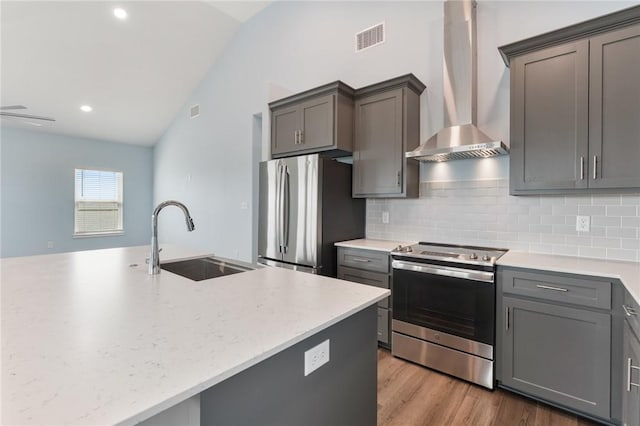 kitchen featuring a sink, lofted ceiling, backsplash, wall chimney exhaust hood, and appliances with stainless steel finishes