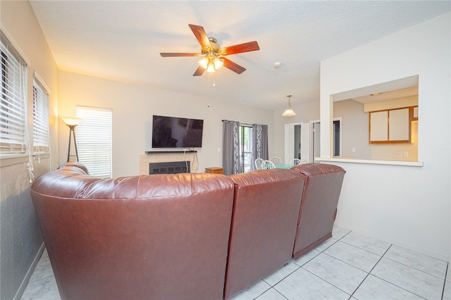 tiled living room with ceiling fan, a textured ceiling, and a tile fireplace