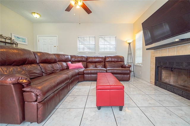 living room featuring ceiling fan, a tiled fireplace, and a textured ceiling