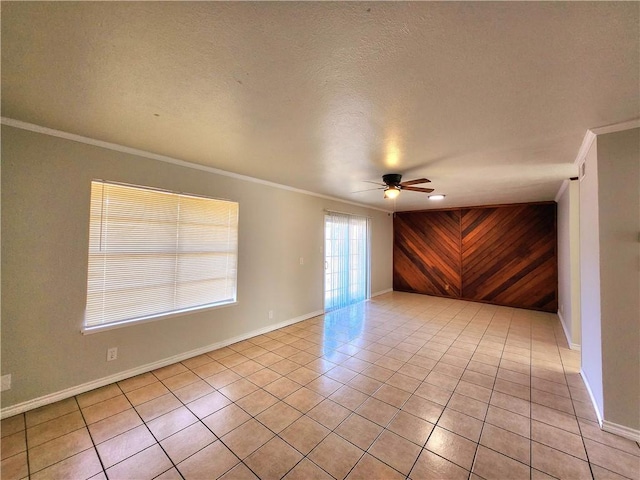 tiled empty room featuring crown molding, ceiling fan, a textured ceiling, and wood walls