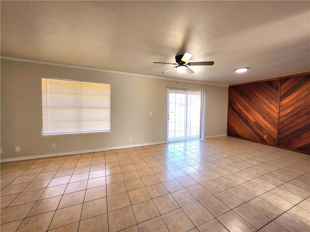 spare room featuring ornamental molding, wooden walls, light tile patterned floors, and ceiling fan