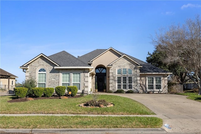 view of front of house with a shingled roof, a front yard, stone siding, and fence