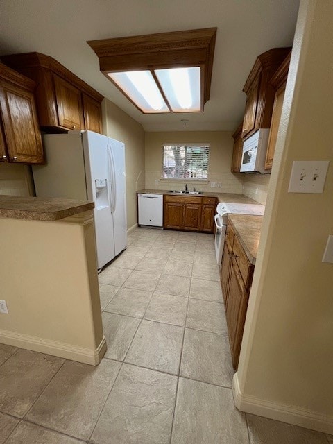 kitchen with kitchen peninsula, white appliances, light tile patterned floors, and sink