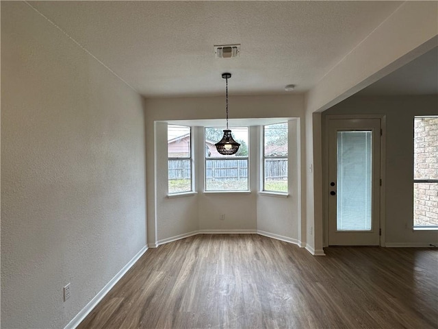 6118 Locke, Corpus Christi, TX 78415 - unfurnished dining area featuring dark wood-style floors, plenty of natural light, a textured ceiling, and a textured wall