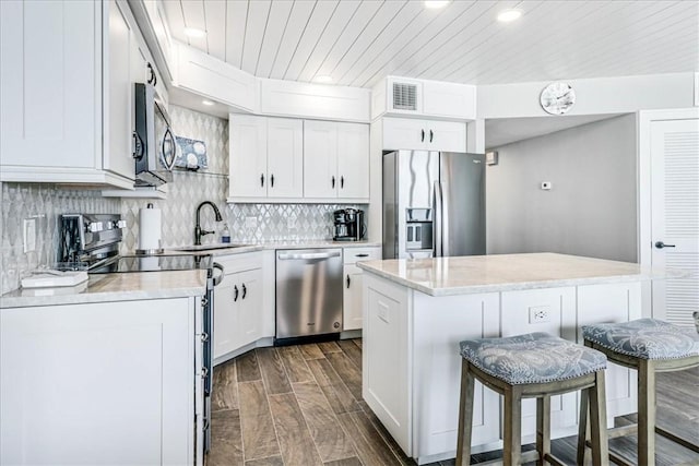 kitchen with a kitchen breakfast bar, light countertops, wood ceiling, a sink, and appliances with stainless steel finishes