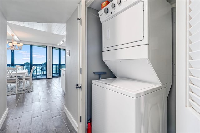 clothes washing area featuring laundry area, wood finished floors, baseboards, a notable chandelier, and stacked washer and clothes dryer