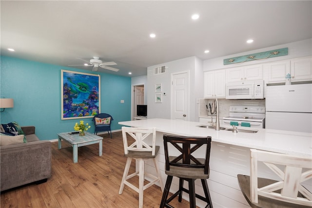 kitchen featuring light wood-type flooring, white cabinetry, backsplash, a breakfast bar area, and white appliances