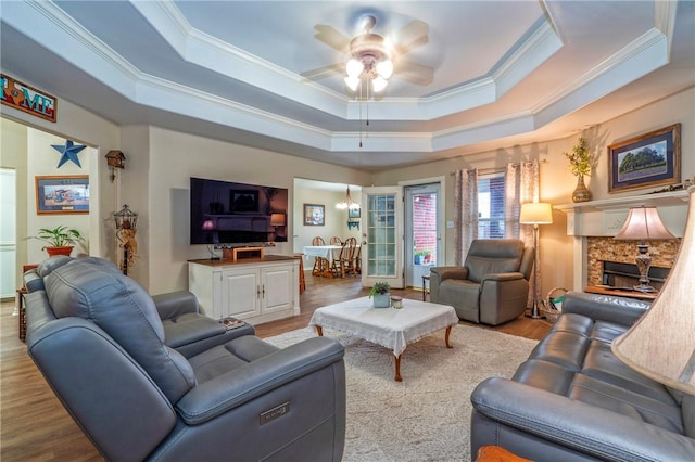 living room with a fireplace, ceiling fan, light hardwood / wood-style floors, a raised ceiling, and crown molding