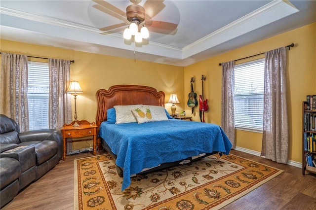 bedroom with multiple windows, hardwood / wood-style floors, and a tray ceiling