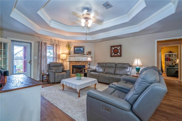 living room with dark wood-type flooring, ceiling fan, ornamental molding, and a raised ceiling