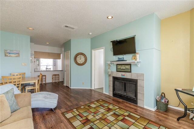 living room featuring hardwood / wood-style floors, a textured ceiling, and a tile fireplace