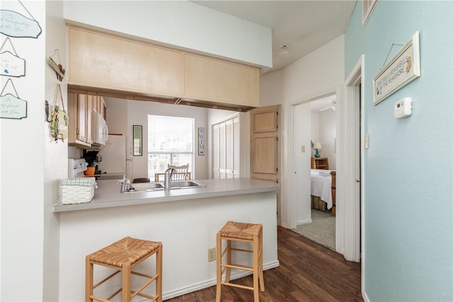 kitchen with a textured ceiling, white appliances, dark hardwood / wood-style flooring, a breakfast bar area, and kitchen peninsula